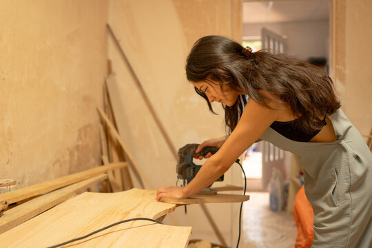 Carpenter using electric jigsaw cutting wooden plank in workshop