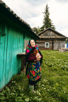 Senior woman holding chicken in front of barn