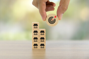 Hand chooses wooden toy block stack with target dart board bullseye and franchise business store for franchising to growth branch expansion and business banking loan or consumer resources service.