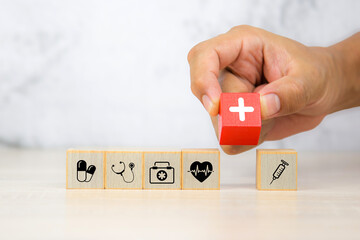 Hand chooses wooden toy block stack with health insurance icons for wellness medical care and healthy for family safety insurances plan or personnel sickness illness treatment concept.