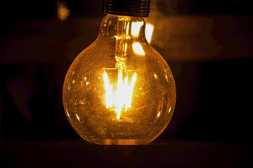 A vintage Edison style light bulb glows with a warm, yellow filament against a dark, moody...