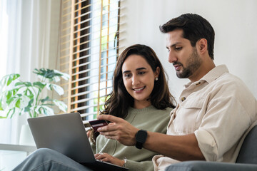 Happy couple using credit card and laptop at home for seamless online shopping experience with smartphone
