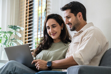 Hispanic couple using computer watching social media and streaming show together at home on the sofa