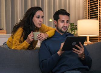 Couple using smartphone together at night browsing social media, watching content and enjoying a cozy digital lifestyle at home.