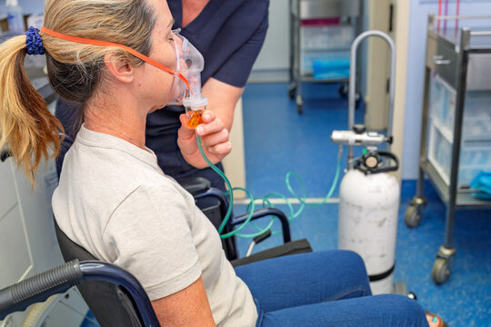 woman in wheelchair with oxygen nebuliser mask being applied by nurse, gp general practice medical healthcare clinic, asthma COPD treatment