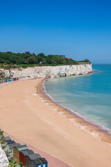 Picturesque Stone Bay in Broadstairs, England, featuring a sandy beach framed by white chalk cliffs under a clear blue sky