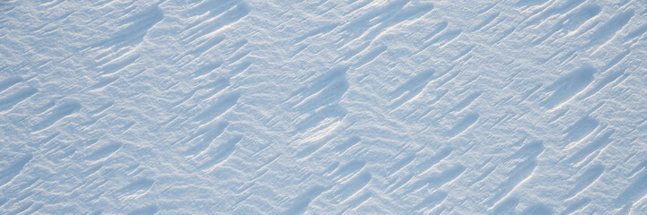 Beautiful winter background with snowy ground. Natural snow texture. Wind sculpted patterns on snow surface. Wide panoramic texture for background and design.
