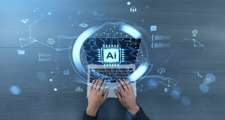 Hands typing on laptop with AI hologram and futuristic digital interface elements on wooden desk background, symbolizing artificial intelligence concept.
