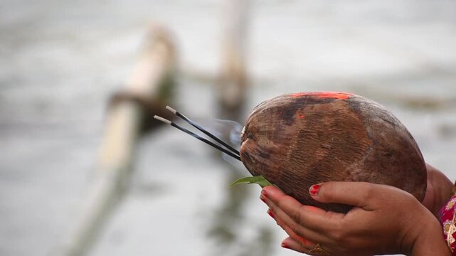 Indian lady with coconut and agarbatti in hand offering to God Sun during Chhath maha parv. no face visible