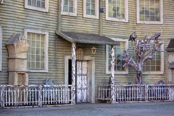 A weathered building facade featuring gothic and horror elements, including grim statues, a white picket fence, and a prominent 