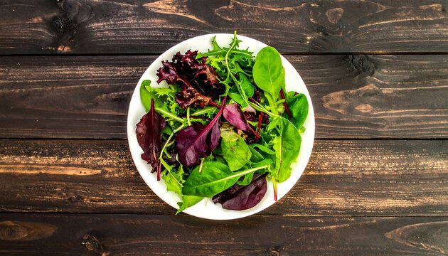 Mixed greens salad on white plate, dark wood table