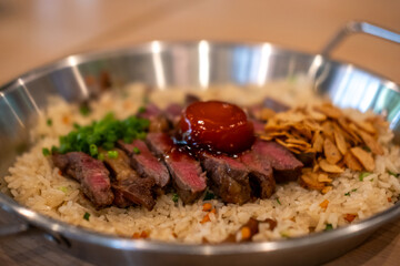 Beef with garlic fried rice, a dish of rice topped with rare beef served with pickled egg yolk with fish sauce on a pan