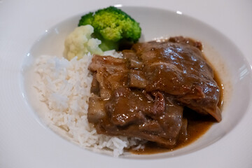 Pork rib with gravy sauce on rice, served on plate