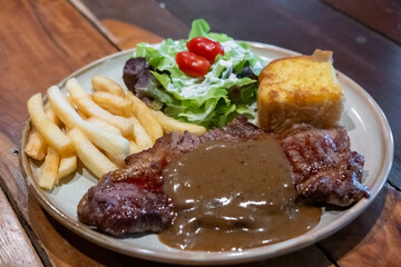 Medium rare meat steak, topped with black pepper sauce on plate with French fries and bread.Medium rare meat steak, topped with black pepper sauce on plate with French fries and bread.