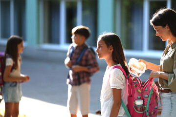 Mother helps daughter with school lunch outside