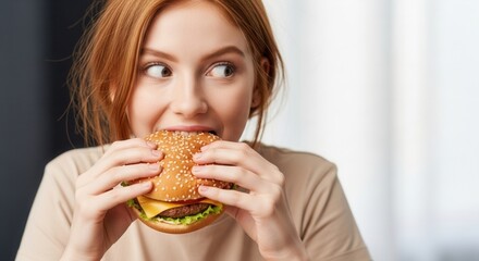 A person with red hair enthusiastically biting into a hamburger holding it with both hands and looking to the side