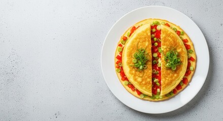 Golden omelet halves garnished with chopped red bell peppers and green onions on a white plate on a speckled grey surface