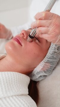 Injection-free mesotherapy or electroporation. Beautician doctor makes client woman face therapy in beauty clinic salon. Girl skin care anti-age spa procedure. Aesthetic cosmetology. Vertical video