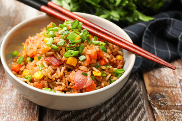 Delicious fried rice with vegetables in bowl and chopsticks on wooden table, closeup