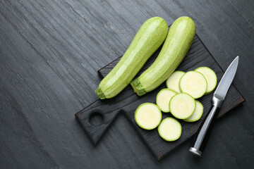 Fresh ripe zucchinis with knife on black textured table, flat lay. Space for text