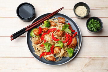 Delicious noodles with meat and vegetables served on light wooden table, flat lay