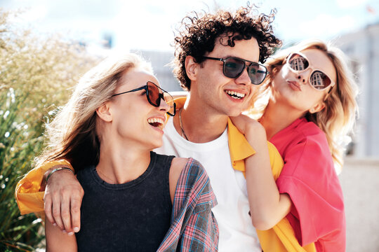 Group of young three stylish friends posing in the street. Fashion man and two cute female dressed in casual summer clothes. Smiling models having fun. Cheerful women and guy outdoors, sunglasses