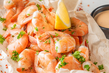 Cooked shrimp served with lemon wedge, dipping sauce, and parsley garnish on parchment paper. Fresh seafood presentation, ideal for culinary, restaurant, or food styling themes.
