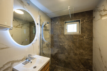 Interior of a bathroom with a glass shower cabin and a large round mirror