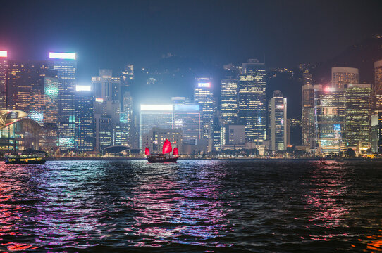 Urban skyline and junk sail at night, Hong Kong harbor