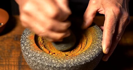 Close-up of hands grinding spices in a traditional mortar and pestle, preparing ingredients for cooking.