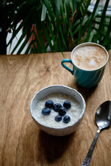 Milk sweet rice pudding with blueberries. Side view. Cappuccino, wooden table, potted flowers