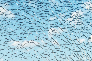 Close-up of cracked tempered glass against blue sky, creating abstract pattern of broken lines and light reflections
