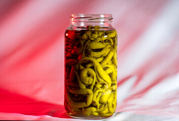 guindillas verdes picantes dentro de un tarro de cristal de pie con fondo blanco y rojo