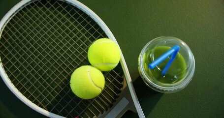 Displaying tennis racket and balls on bench, with lidded green drink cup, blue straws, copy space