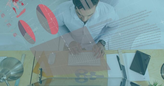 Typing Asian male leaning over office desk and viewing charts overlay, with keyboard mouse lamp