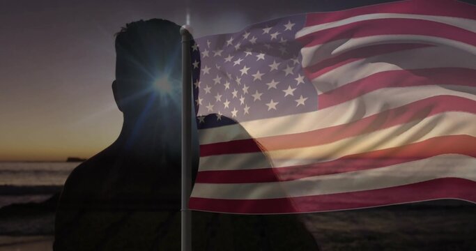Silhouetted man holding waving American flag on shore at sunset, with sunburst and ocean waves - Powered by Adobe