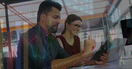 Reviewing professionals in business attire in open-plan office, overlaying digital graphs on tablet