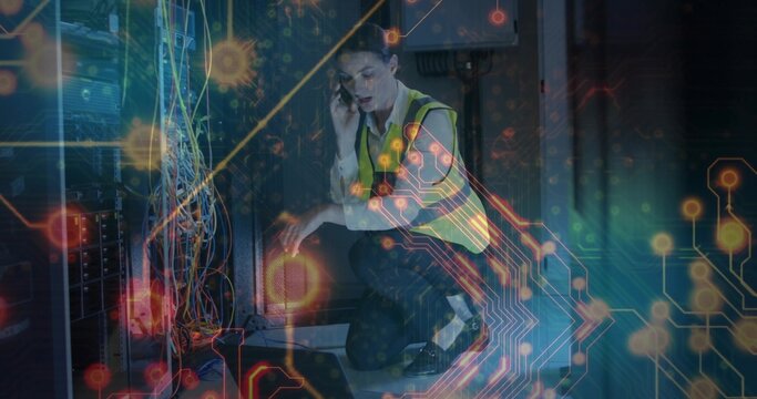 Kneeling network tech troubleshooting switches in data center in safety vest, with phone and laptop