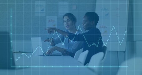 Analyzing data trends on silver laptop by two businesswomen in office meeting room, graph overlay