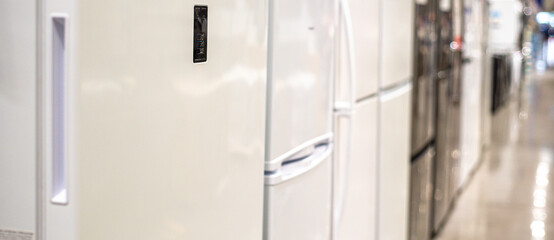 Panorama view top-freezer and side-by-side refrigerators lined up in showroom with polished...