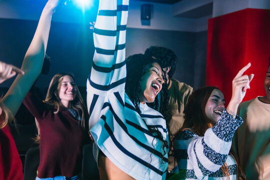 Group of friends enjoying a lively music concert, dancing and raising their hands in excitement while celebrating togetherness and joy