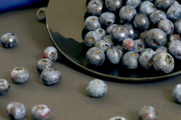 Blueberry still life on black plate with dark background and blue fabric