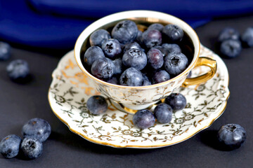 Blueberry still life in vintage porcelain cup with saucer on dark blue background