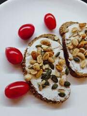 Whole grain toast with cream cheese, seeds, peanuts and cherry tomatoes. Homemade snack with whole grain bread topped with cream cheese, peanuts and mixed seeds, served with fresh cherry tom
