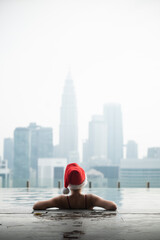 Tourist enjoying christmas vacation in infinity pool overlooking kuala lumpur city skyline