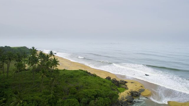 Aerial drone panning shot waves crashing into golden sand of Kappil bekal beach into a backwater inlet under the monsoon overcast sky at this popular tourist place