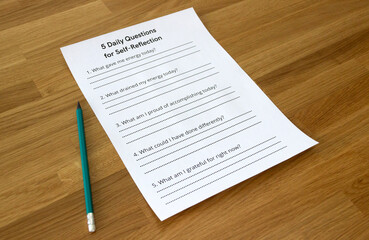 Blank sheet titled '5 Daily Questions for Self-Reflection', self-reflection concept, self-awareness concept, isolated on wooden background