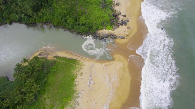 aerial drone shot descending straight down showing waves pushing water into backwater inlet in Kappil bekal beach with rocks to the side and blue green water showing the beauty of god's own country