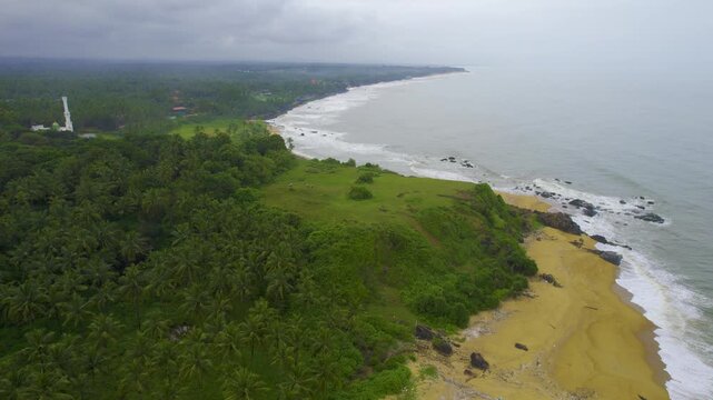 Aerial drone shot orbiting people walking on cliff near Kappil bekal beach in Kerala with a mosque and buildings in the background showing the natural beauty in India