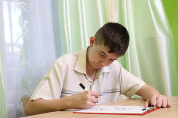Naklejka premium Boy carefully draws holding a black marker and leaning over the sheet of paper.